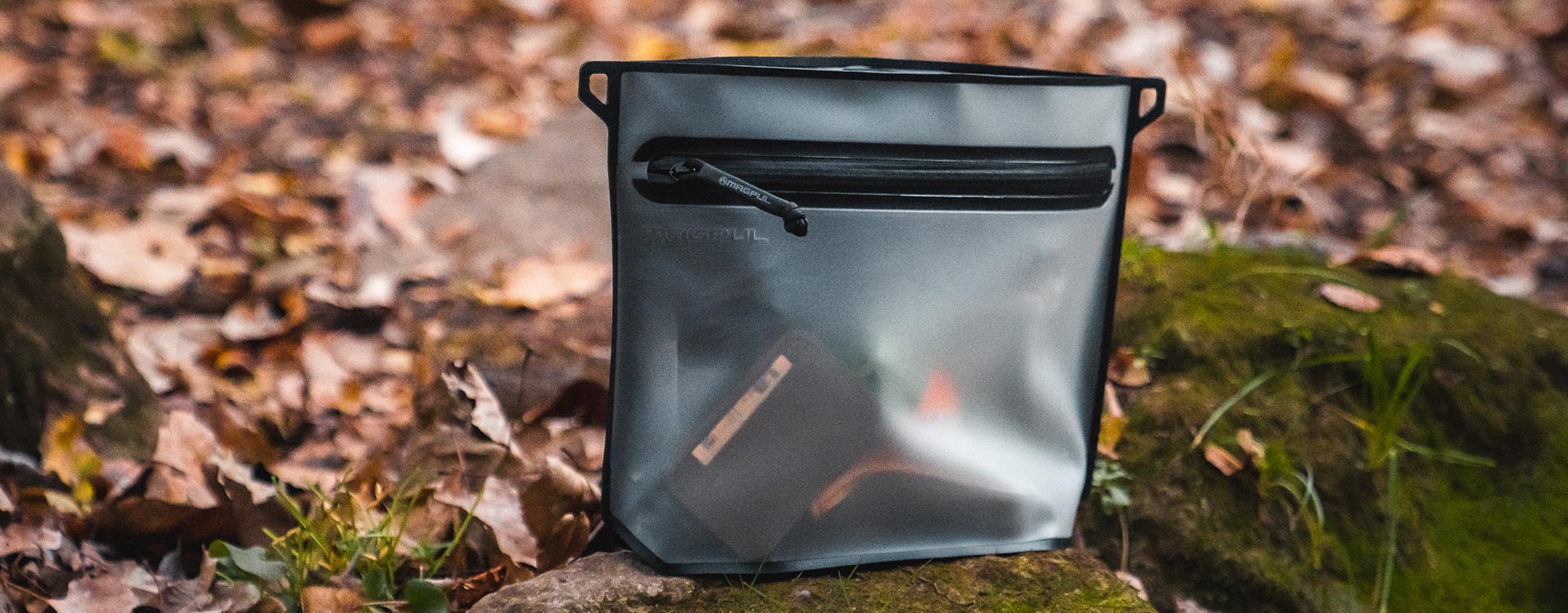 Magpul DAKA Large Volume Pouch outdoors sitting upright on a mossy rock, filled with a variety of goods